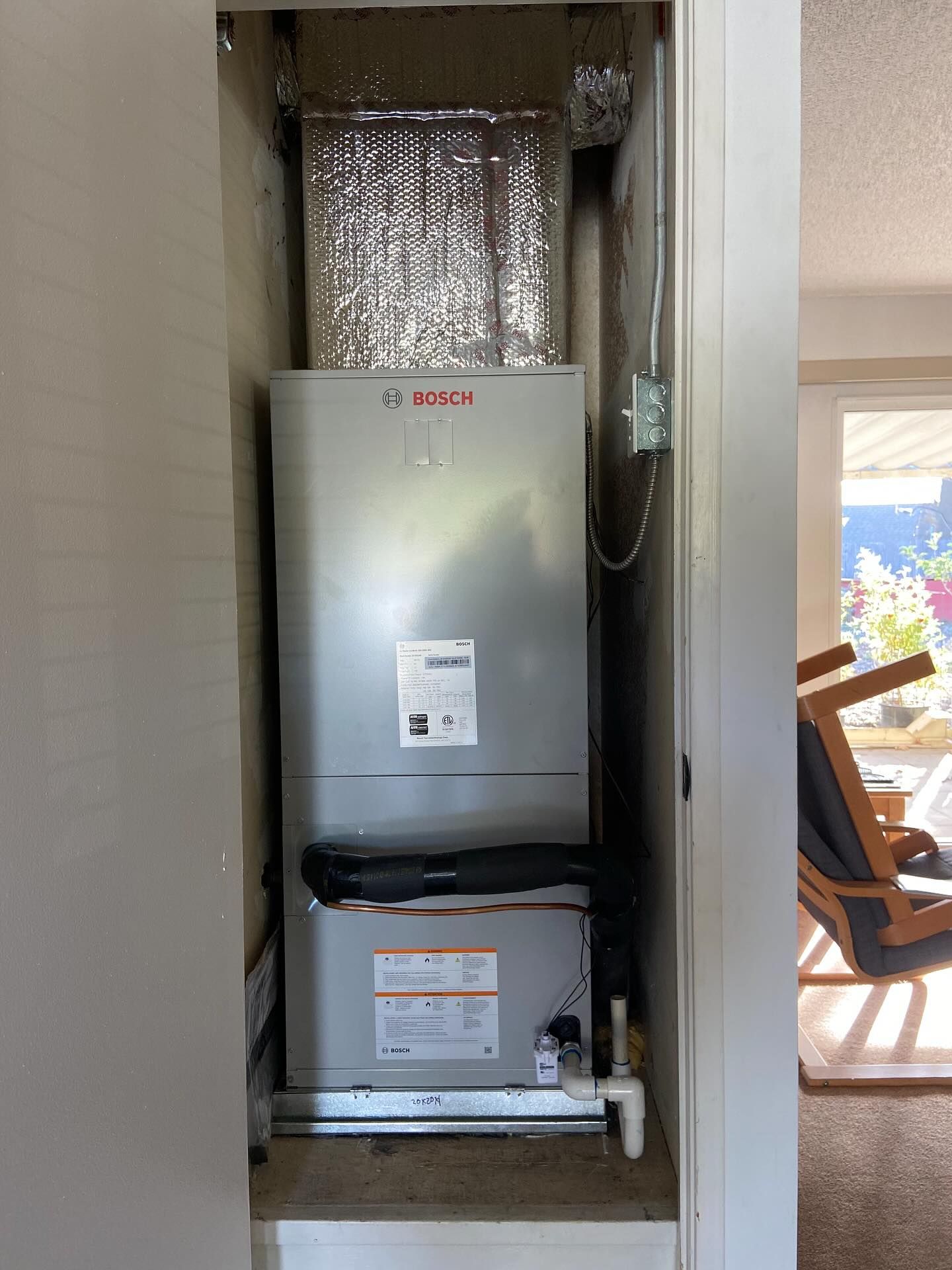 Wall-mounted HVAC unit in a utility closet with exposed ductwork and piping