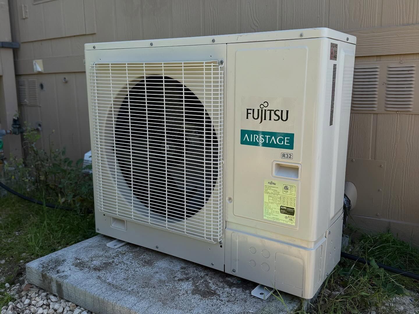 Fujitsu air conditioner outdoor unit beside a building, with fan grille and compressor housing.