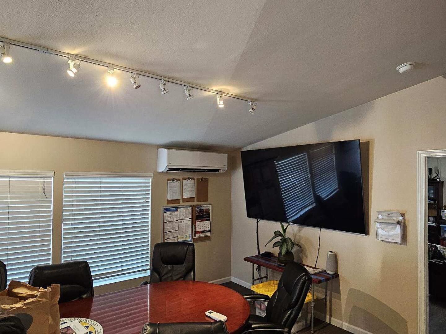 Living room with sectional sofa, wall-mounted TV, blinds, and track lighting