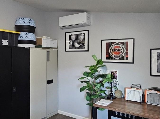 Small office corner with cabinets, wall art, air conditioner, plants, and a desk with files and decor.