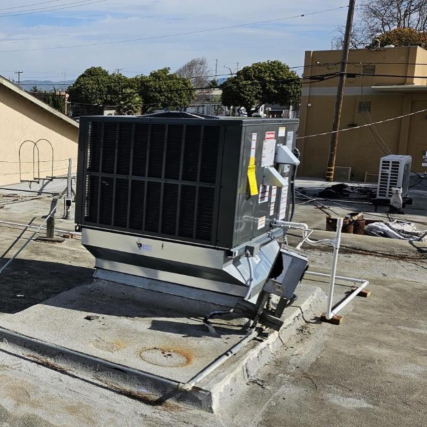 Damaged rooftop HVAC unit on a concrete pad with debris and nearby rooftop equipment