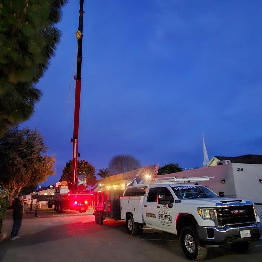 Utility trucks and a crane lift near a building at dusk, with red lights glowing on the street.