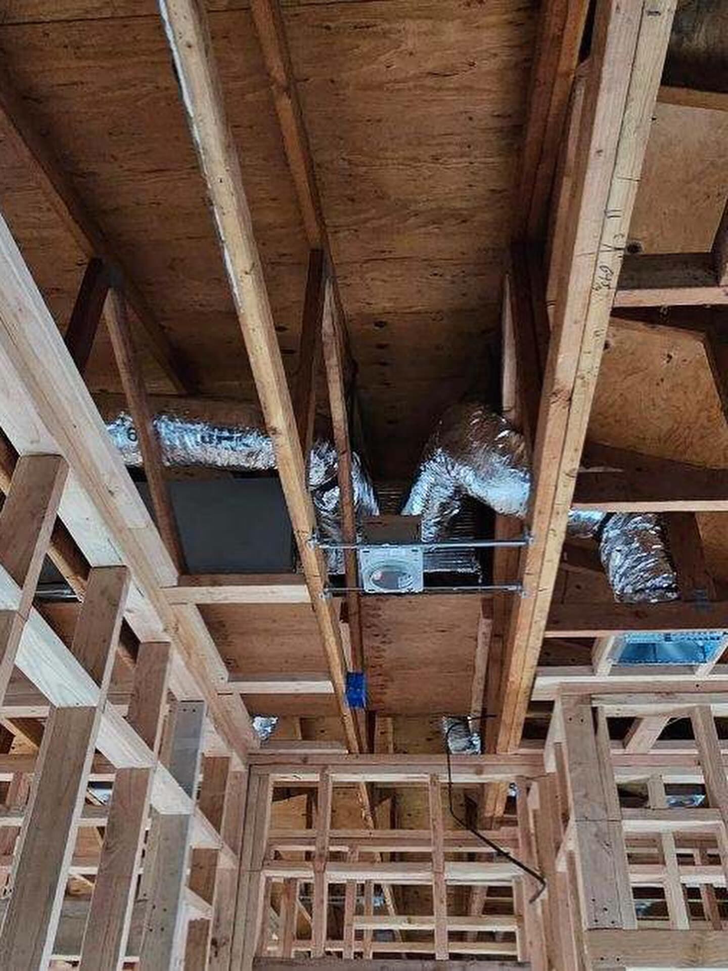 Interior of a building under construction with exposed wooden framing, joists, and insulation in the ceiling.