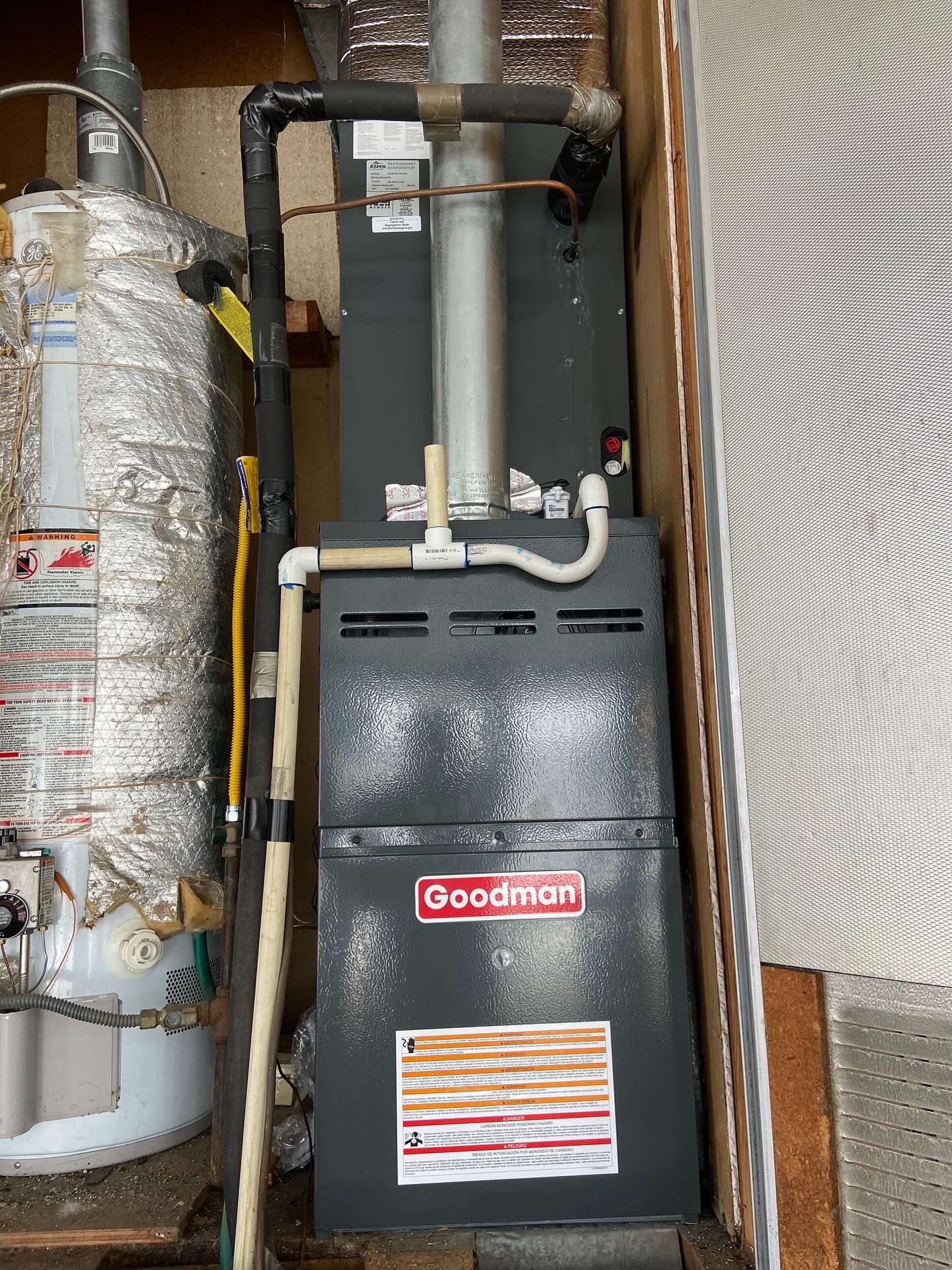 Goodman furnace with exposed pipes and ductwork in a utility closet