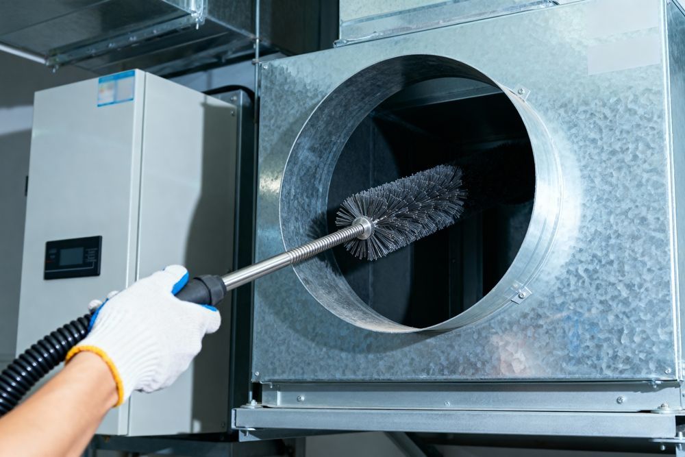 Person cleaning a large metal ventilation duct with a rotary brush tool