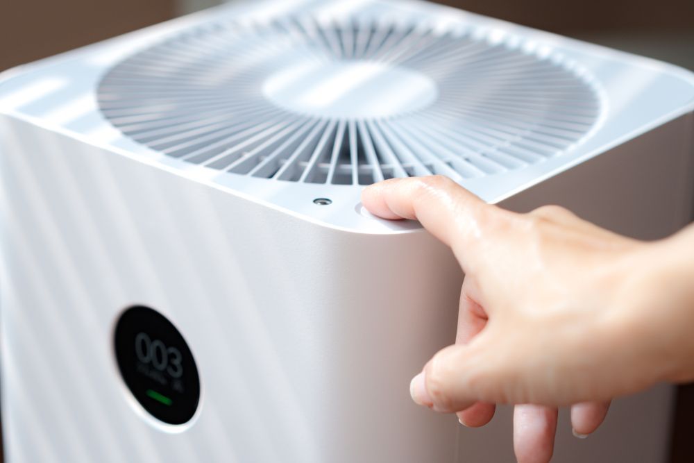 Hand turning on a white cube air purifier with a round digital display on top