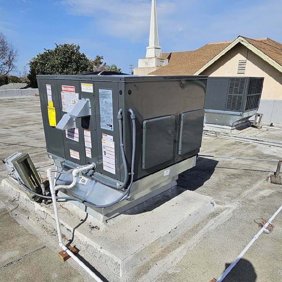 Roof-mounted HVAC unit on a flat rooftop with electrical conduit and a church steeple in the background