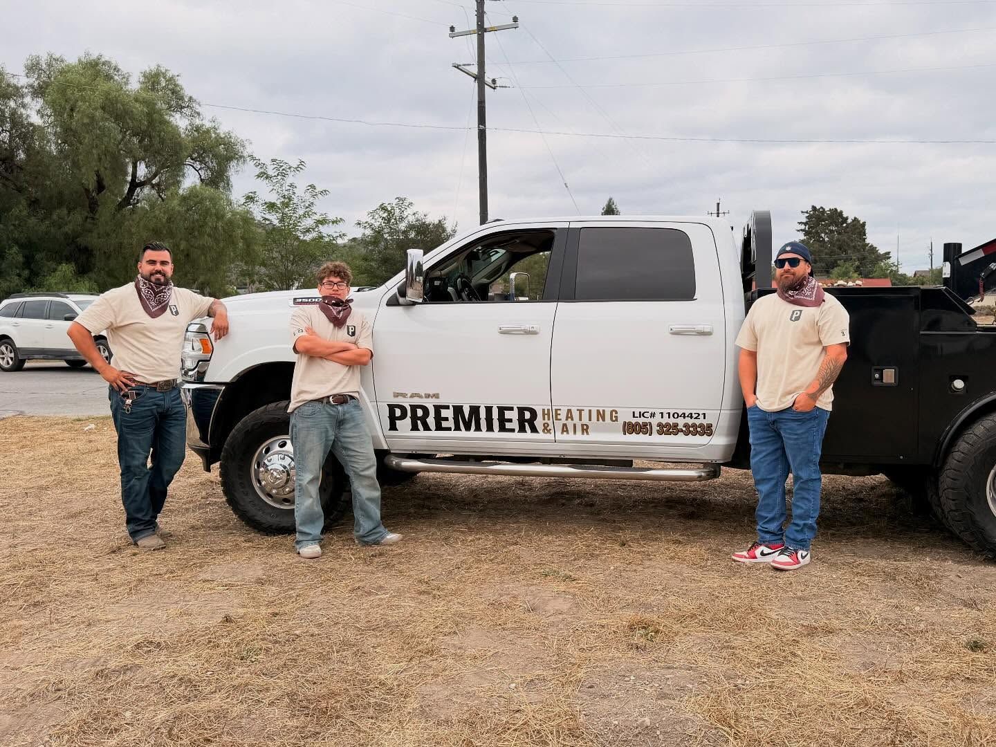 Three people stand beside a white Premier truck and black trailer on a gravel lot.