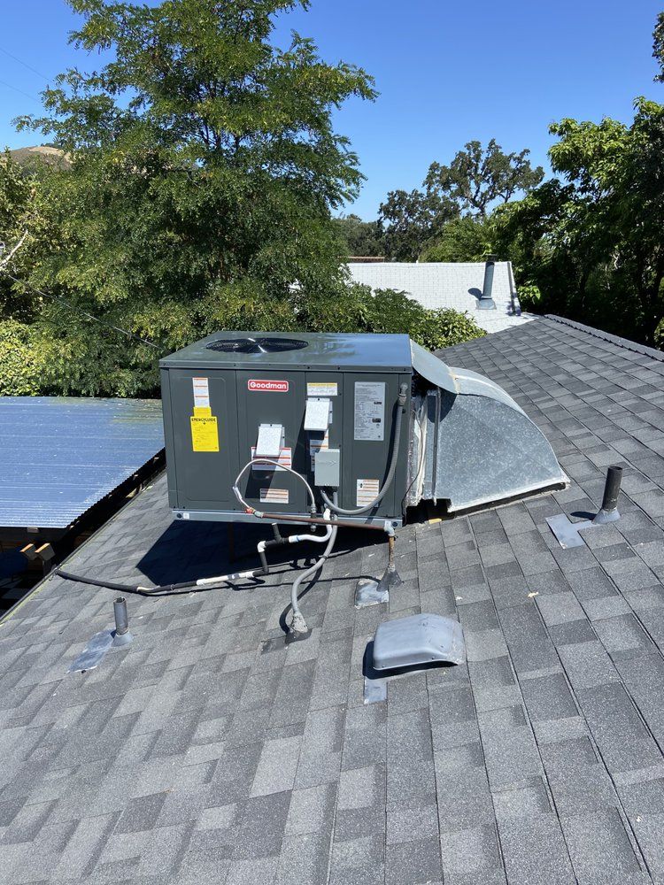 Roof-mounted HVAC unit on a gray shingle roof with trees and blue sky in the background