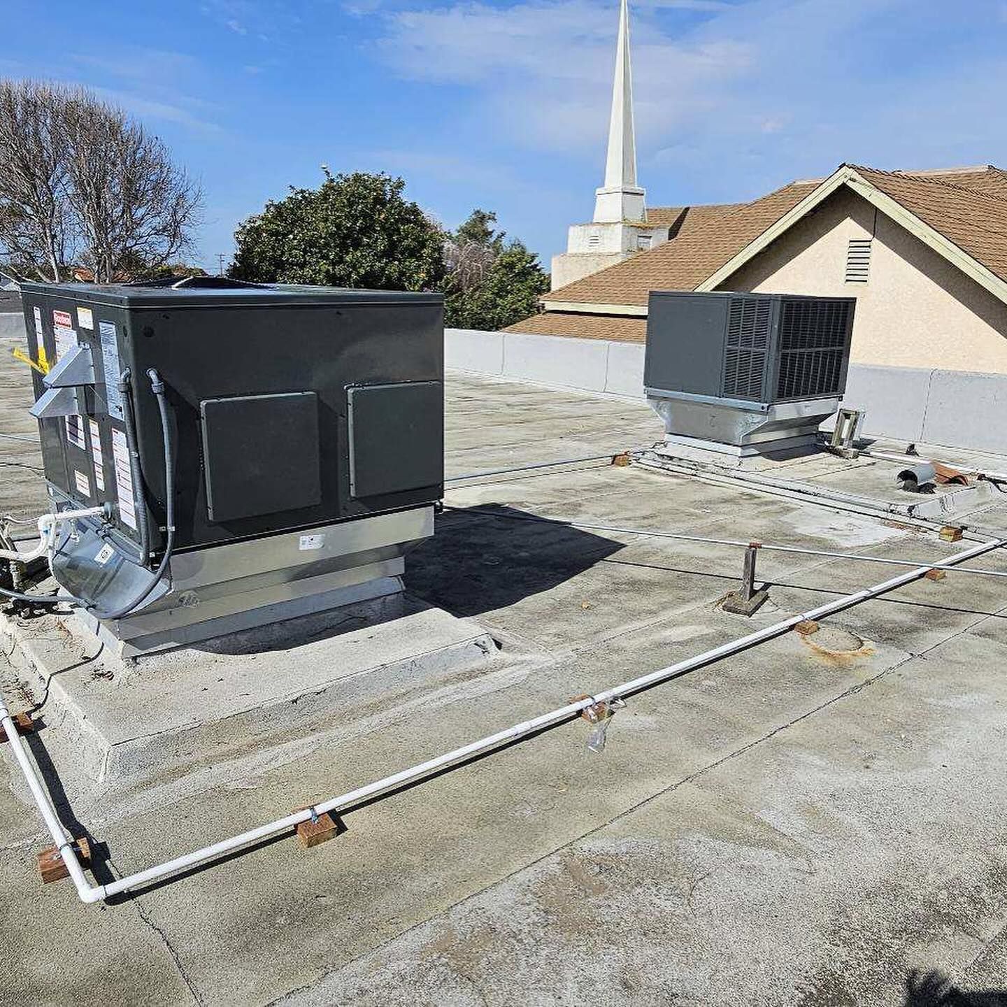 Rooftop HVAC units and ductwork on a flat commercial roof with a church steeple in the background