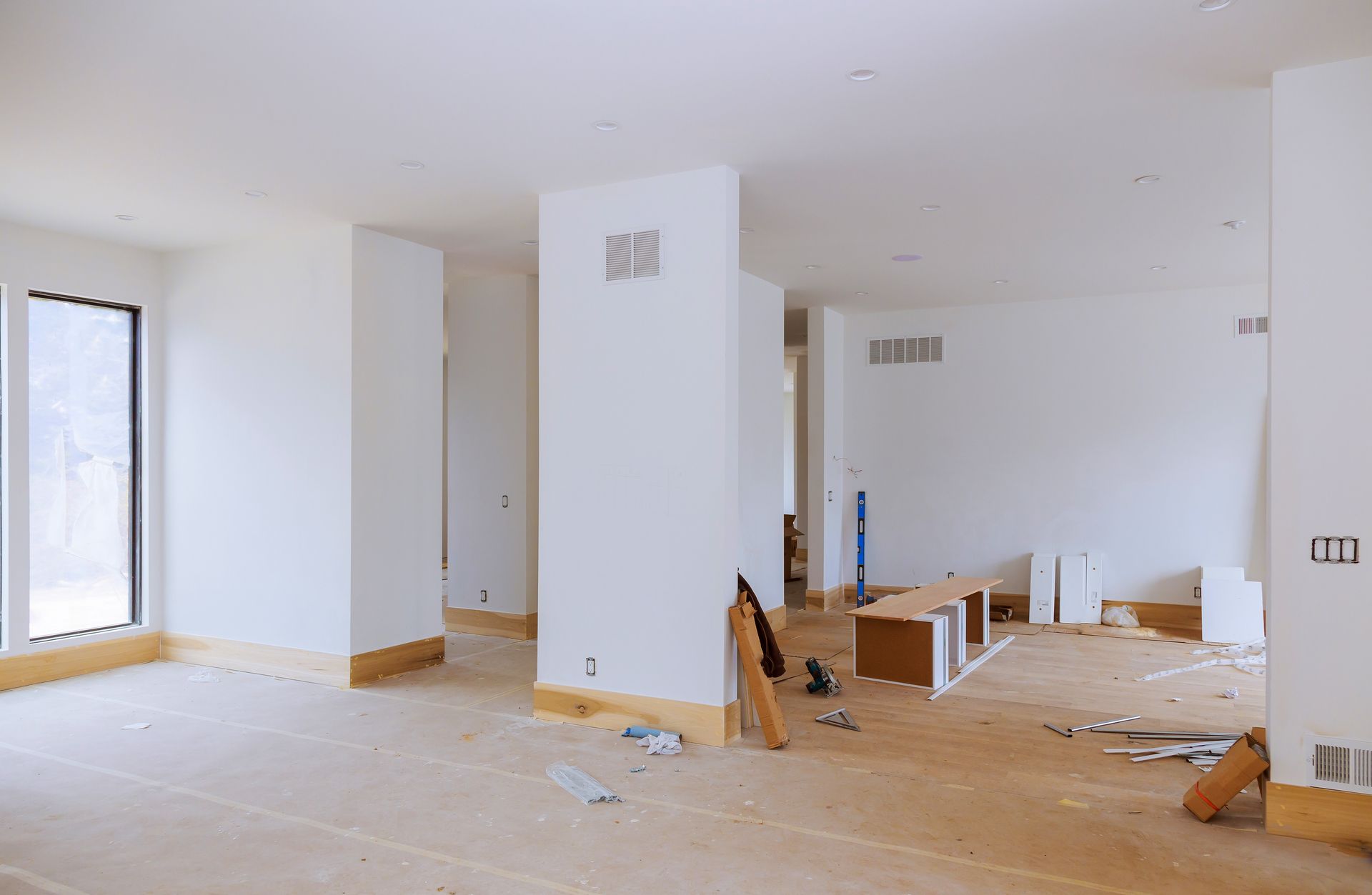 Empty room under renovation with drywall, tools, and debris on a wooden floor