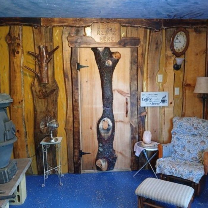 Rustic room with wooden walls and door. Includes an armchair, clock, and small table.