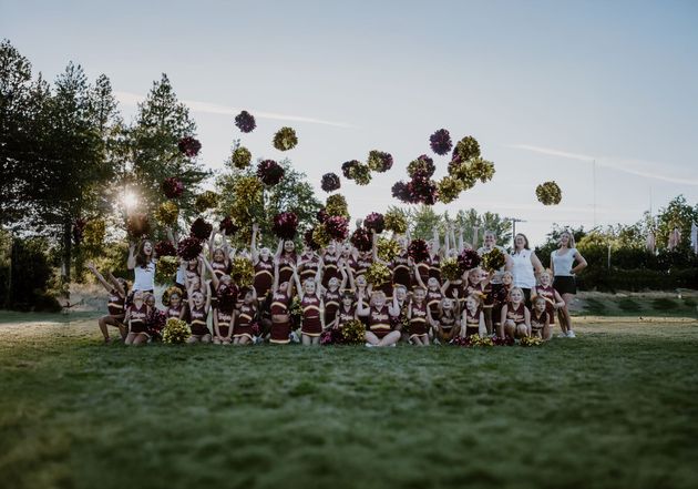 Cheerleader in red uniform performs a backbend on a green and red football field.