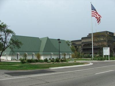 Government building with green roofs and a U.S. flag beside a road and parking lot