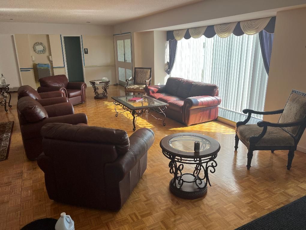 Spacious living room with leather chairs, a sofa, coffee table, and large curtained windows.