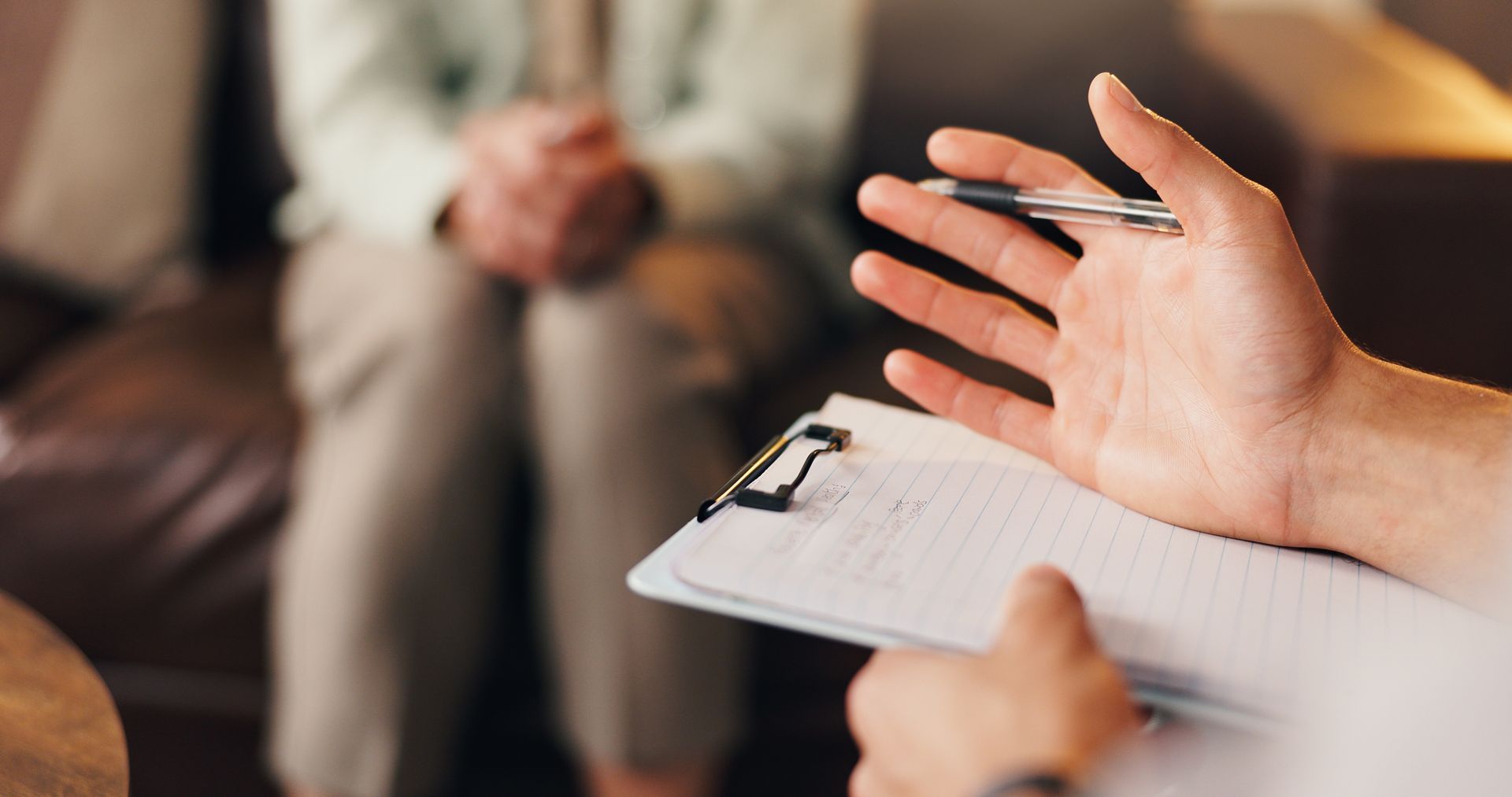 Hand gesturing during a counseling session beside a clipboard, with a seated person in the background