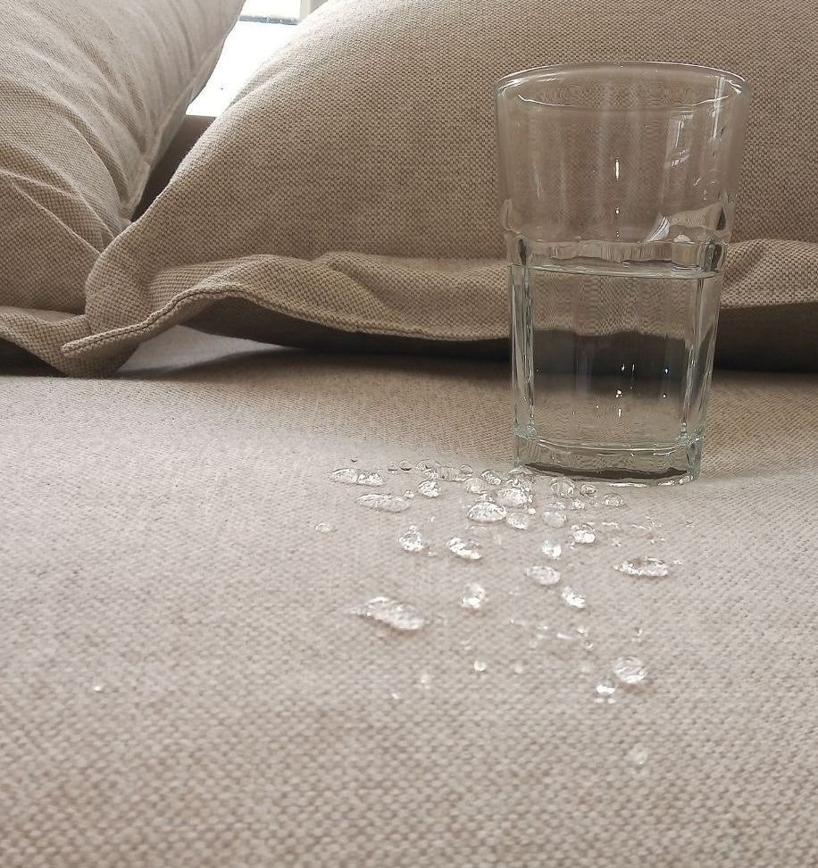 A glass of water sits on a couch next to a pillow