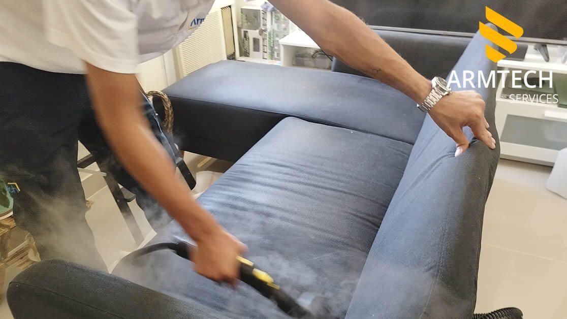 A man is cleaning a blue couch with a steam cleaner