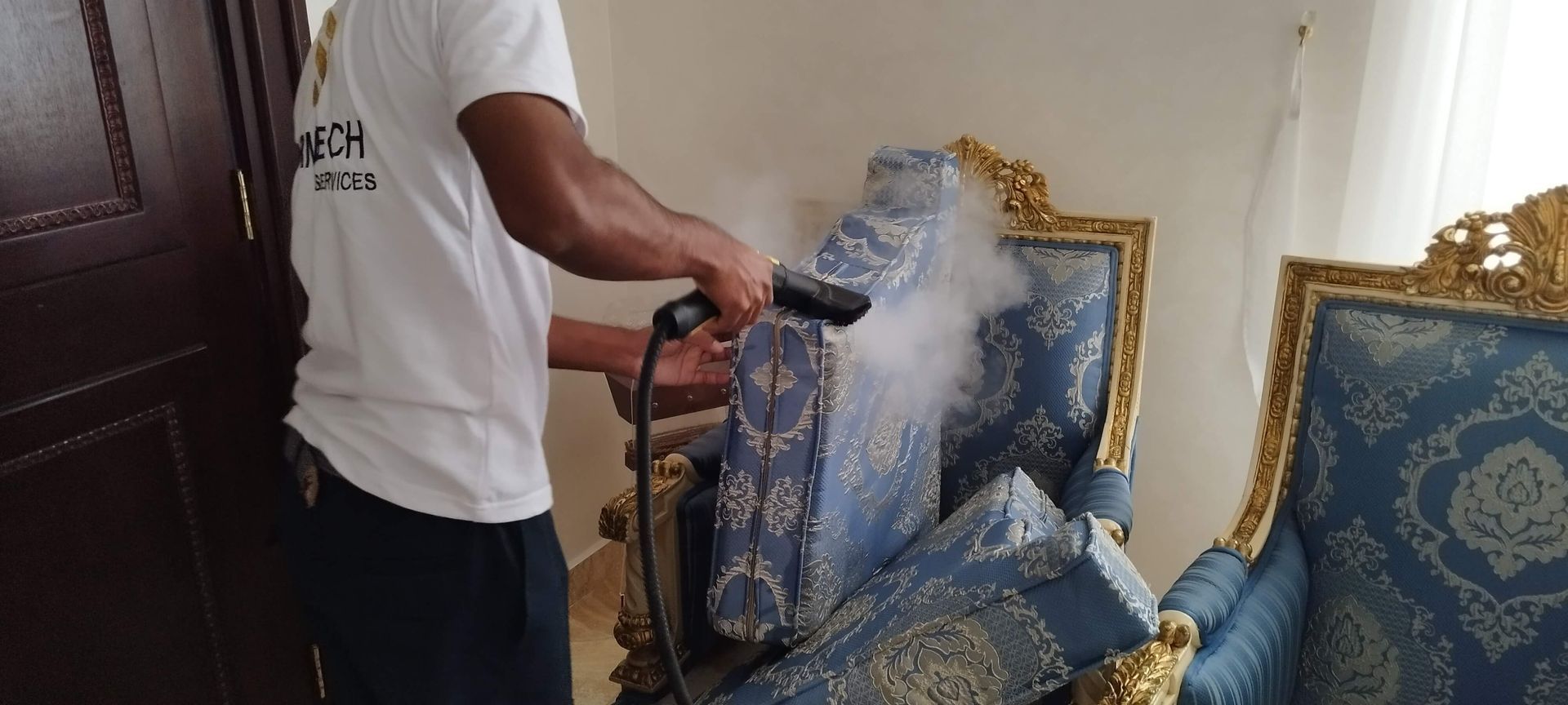 A man is cleaning a chair with a steam cleaner.