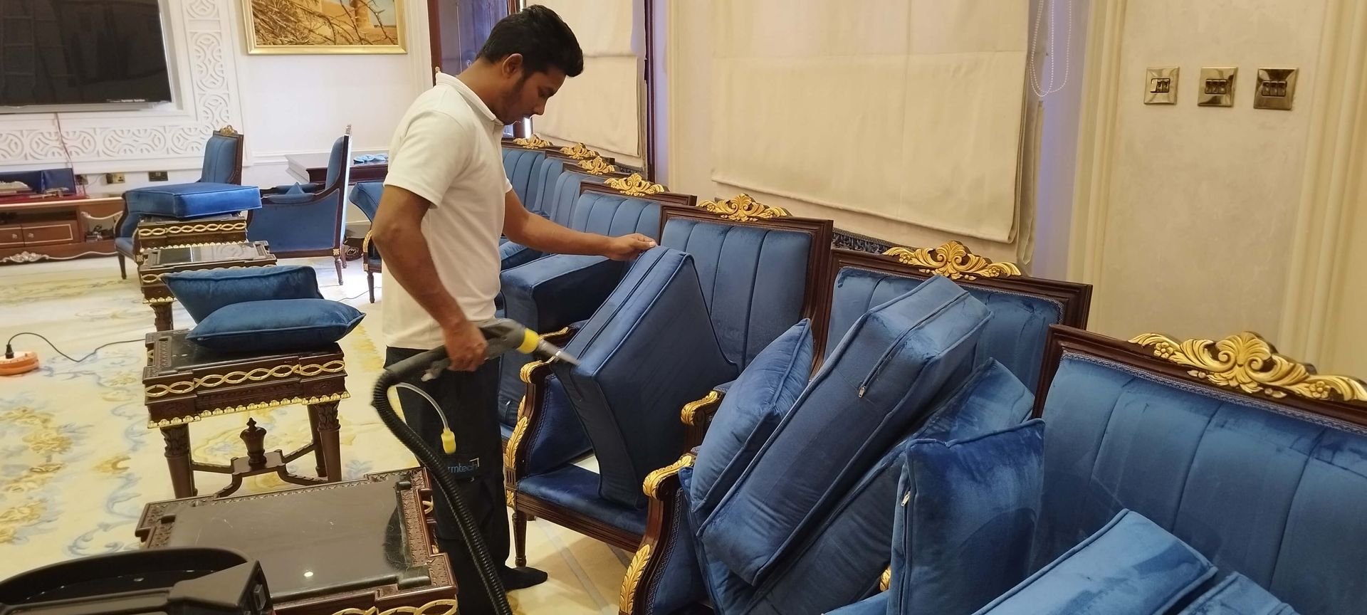 A man is cleaning a couch with a vacuum cleaner