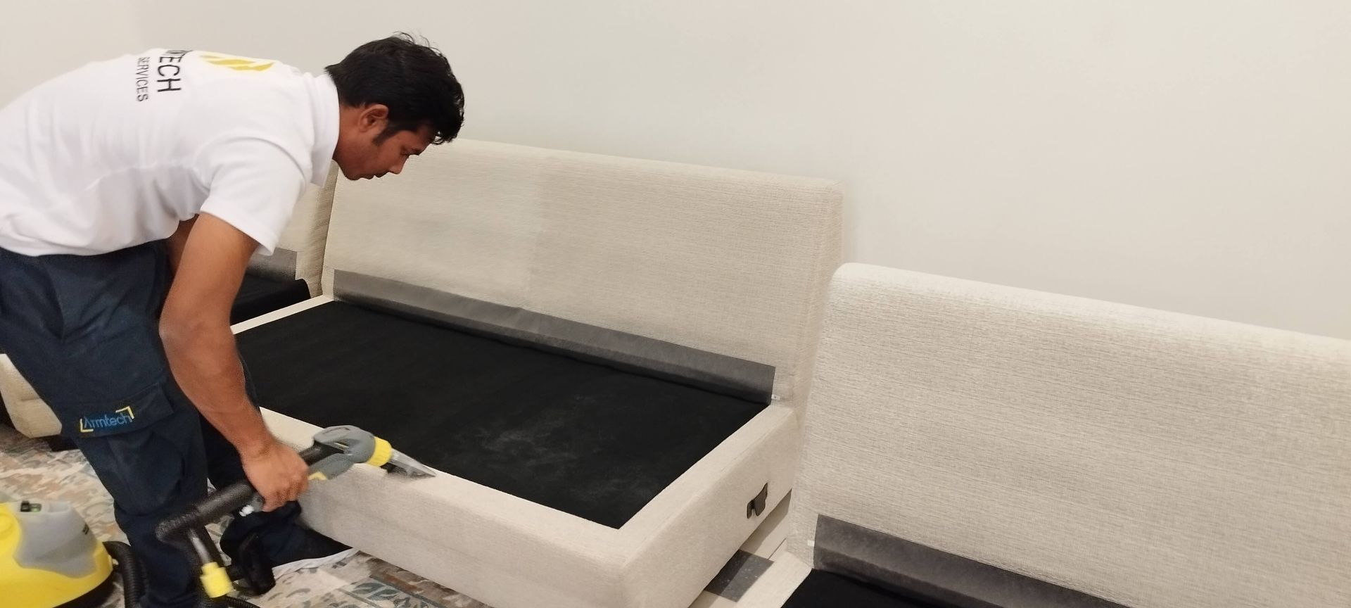 A man is cleaning a couch with a vacuum cleaner.