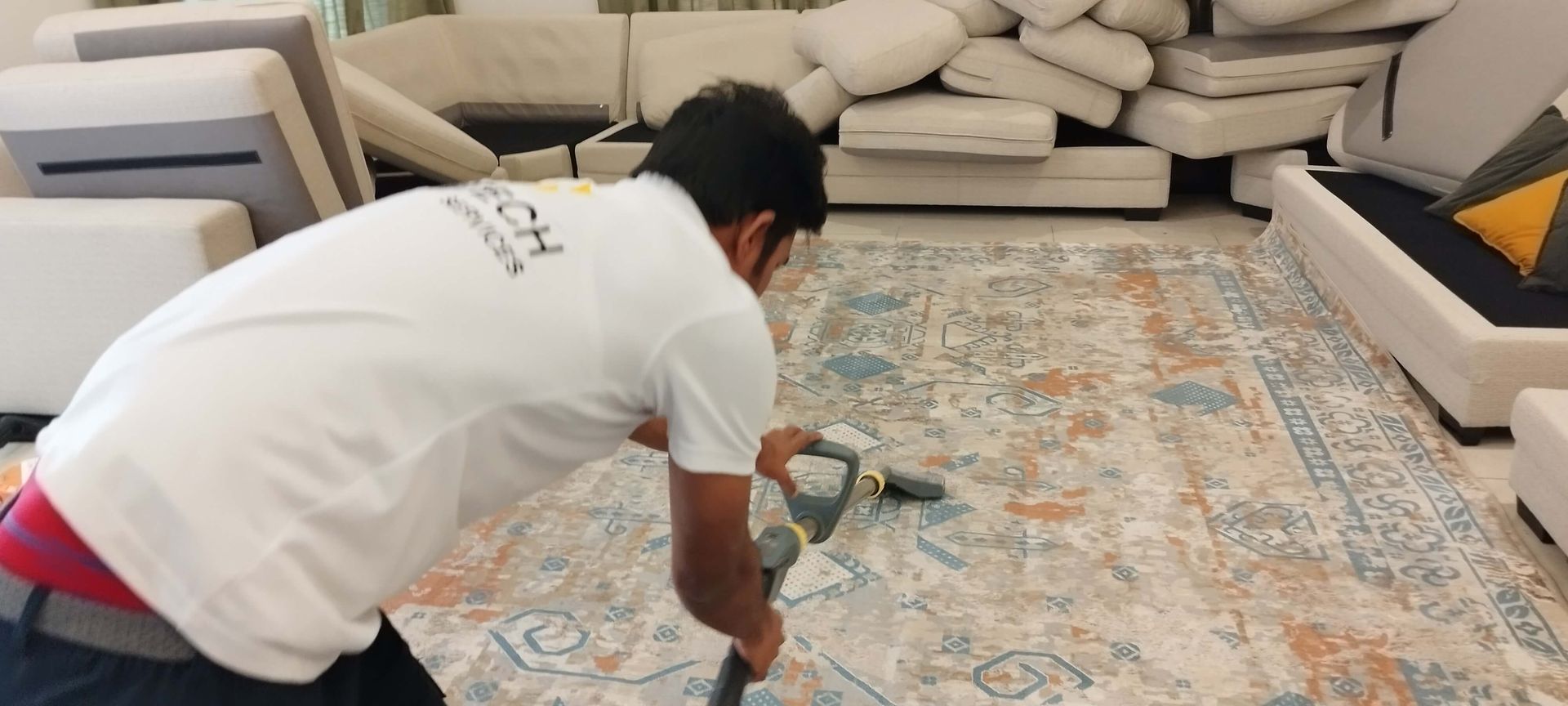 A man is cleaning a rug in a living room with a vacuum cleaner.