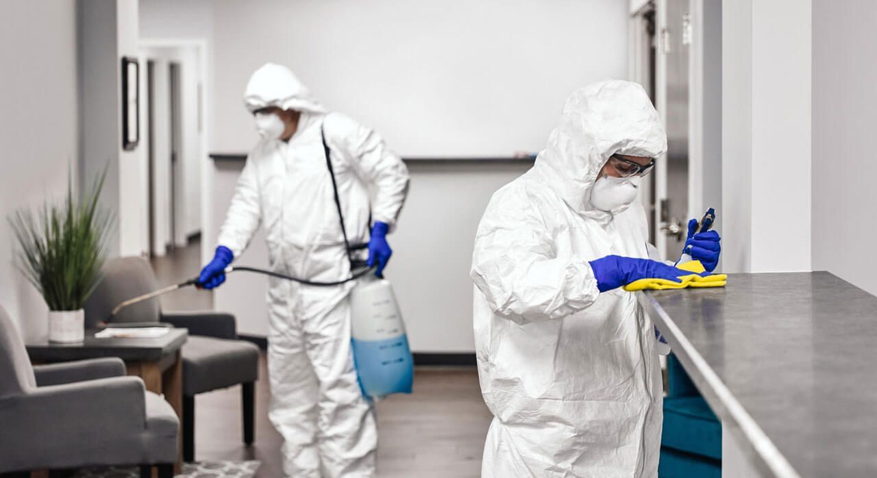 Two people in protective suits are cleaning an office.