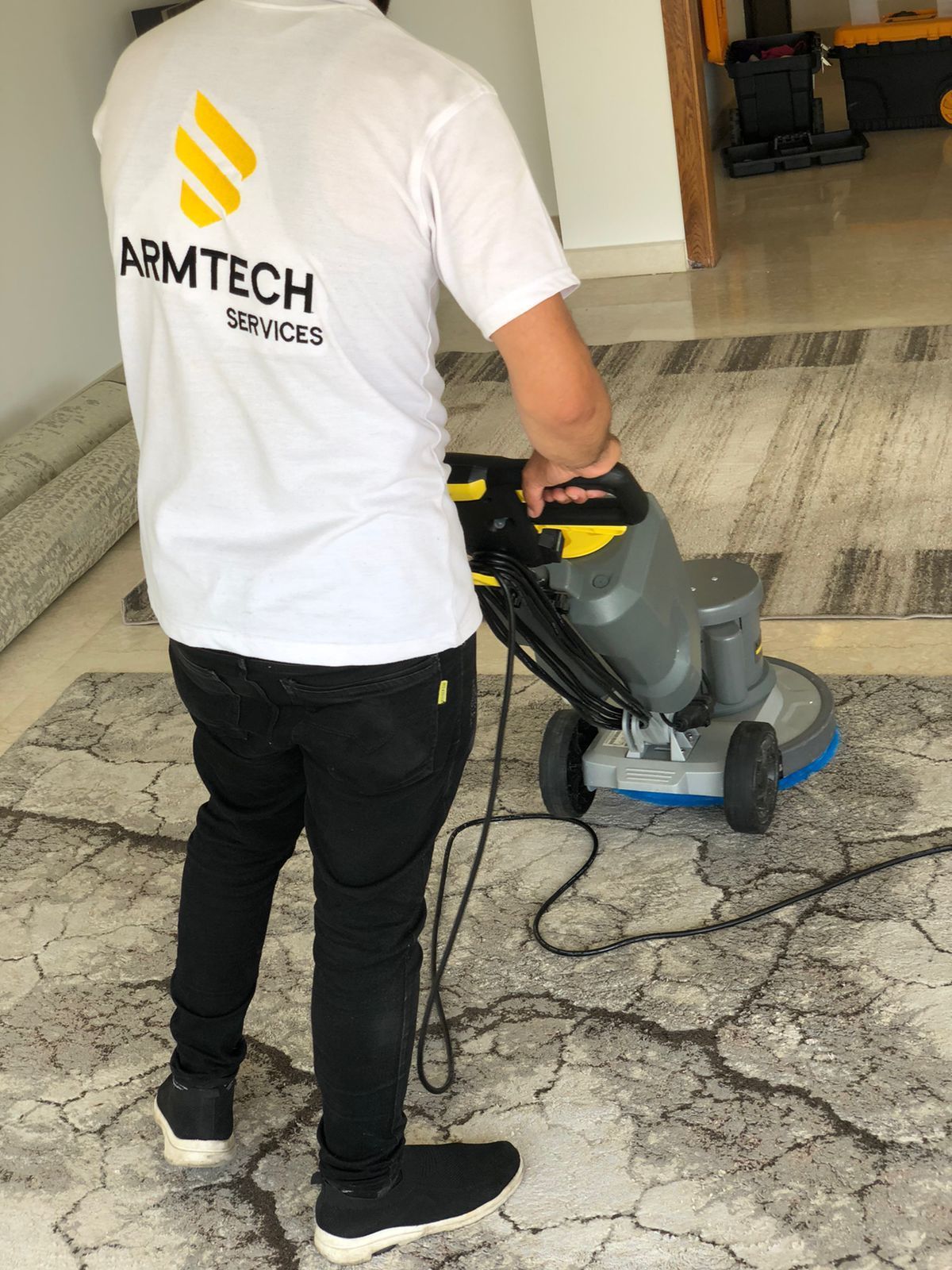 A man wearing a white shirt that says armtech services is cleaning a rug