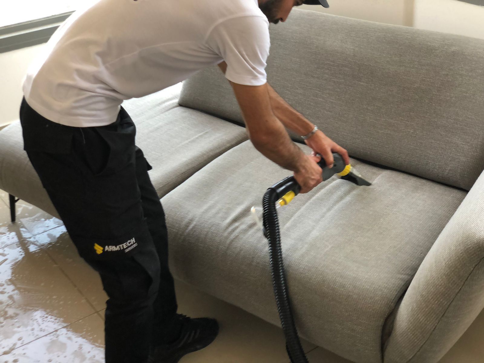 A man is cleaning a couch with a vacuum cleaner