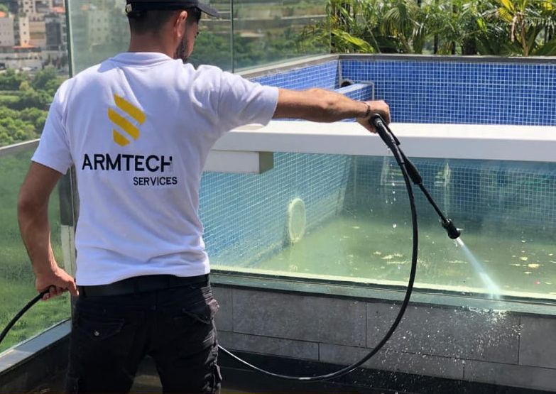 A man wearing an armtech shirt is spraying water on a pool