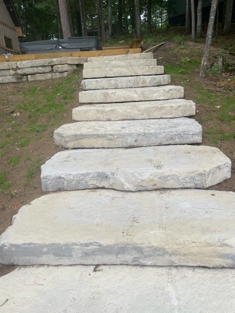 Stone steps leading up a backyard patio, bordered by grass and trees.
