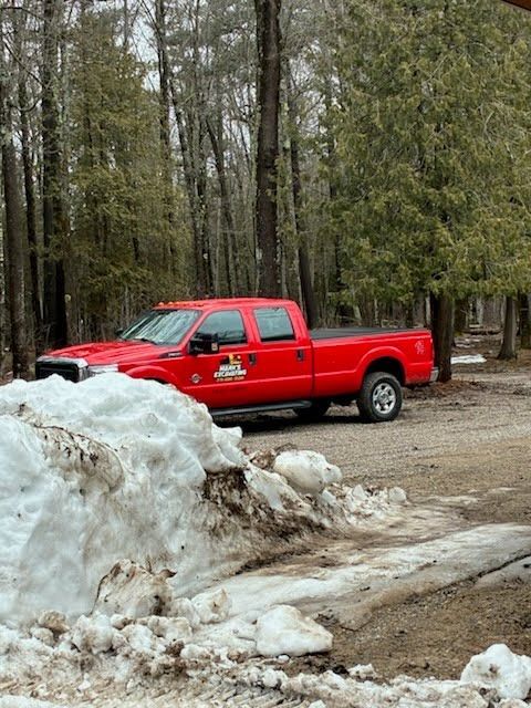 Red pickup truck parked beside a dirty snowbank in a wooded area