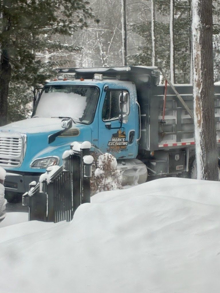 Blue dump truck parked in deep snow beside a wooded road