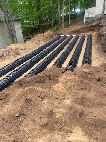 Black corrugated pipes laid in a sandy trench at a wooded construction site