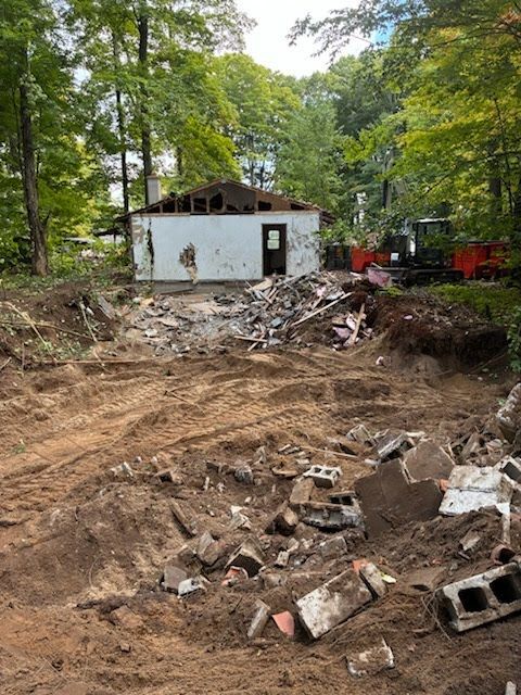 Flood-damaged yard with mud, scattered debris, and a small white building amid trees