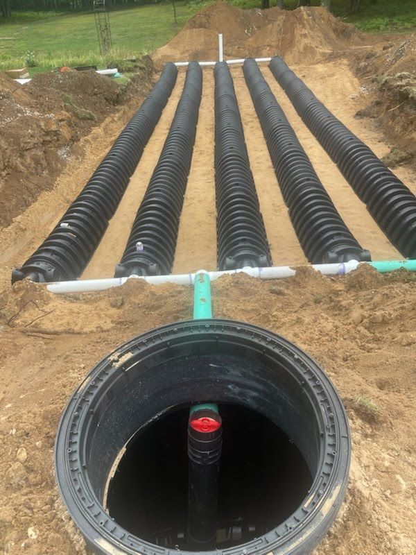 Black corrugated drainage pipes installed in a trench, leading to a large round pipe opening in the foreground