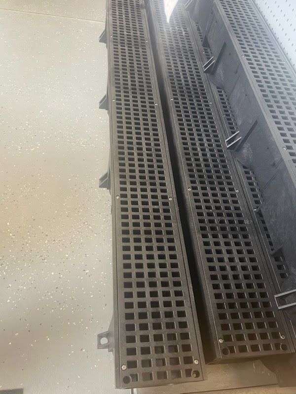 Metal drainage grates along a concrete walkway indoors