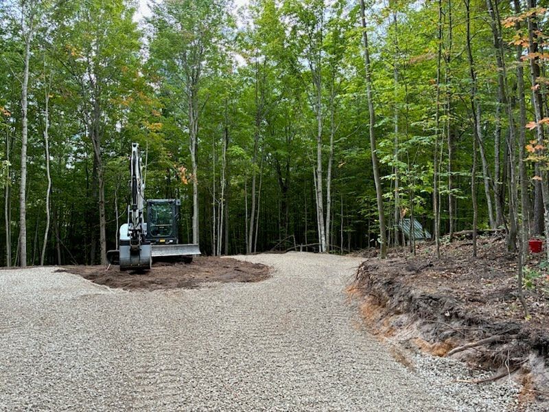 Excavator on a gravel road clearing land in a green forest clearing