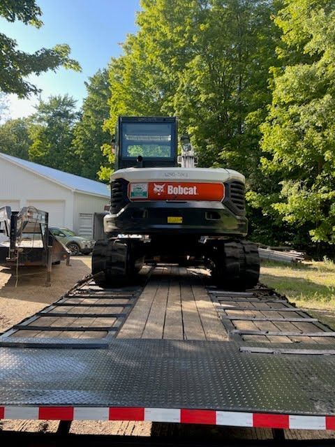 Bobcat excavator on a trailer in a driveway beside a house and trees