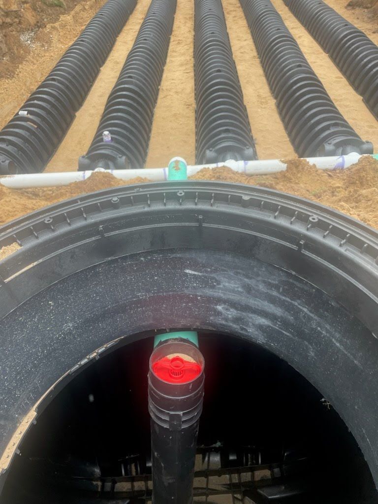 Large black drainage pipe with red-capped connector at construction site, with corrugated pipes in the background