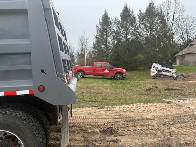 Gray dump truck, red pickup, and damaged white SUV on a muddy roadside near trees and a house
