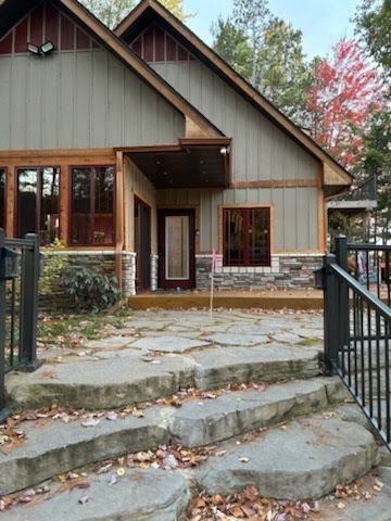 Front view of a rustic house with stone steps, wood trim, and a black metal gate in autumn.