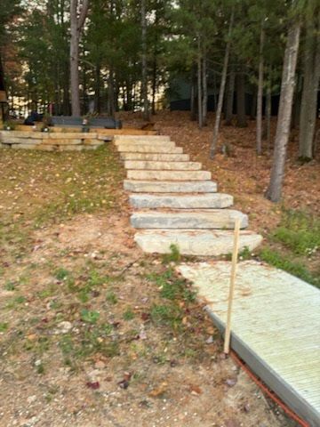 Stone steps leading up a wooded slope, with a paved path and railing in the foreground.