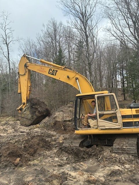 Yellow CAT excavator digging in a muddy construction site with bare trees in the background