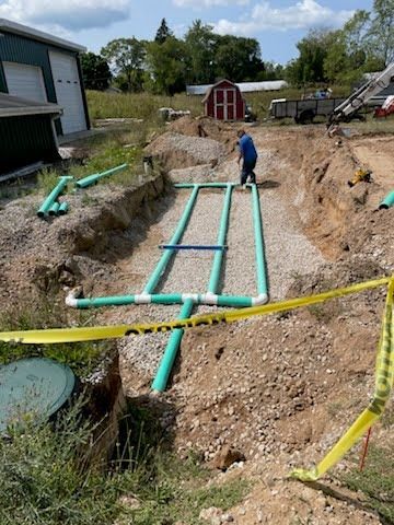 Person working in a dirt trench beside green PVC pipes at a house construction site
