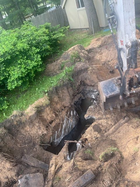 Open trench beside a house, with exposed dirt and an excavator working near a utility pole.