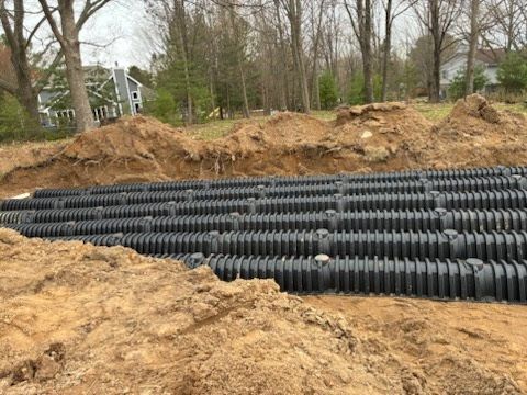 Rows of black drainage pipes laid in a dirt trench at a wooded construction site