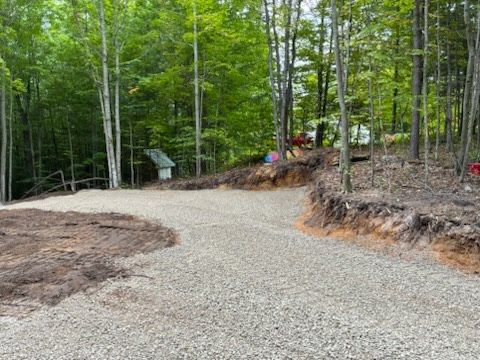 Gravel path curving through a wooded park with trees and a small signpost on the left.