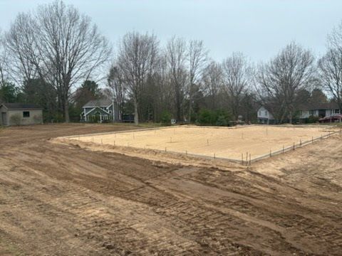 Cleared dirt lot with leveled sandy area and bare trees in a suburban neighborhood