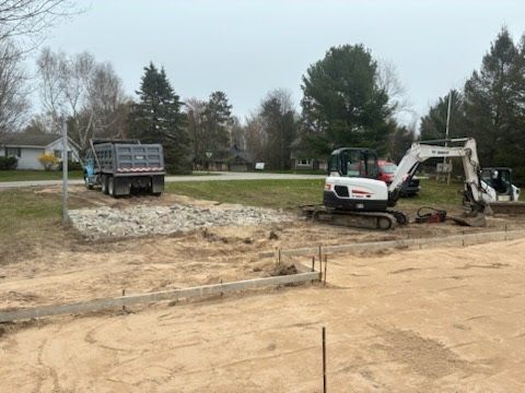 Construction equipment working on a dirt lot beside a truck in a suburban yard